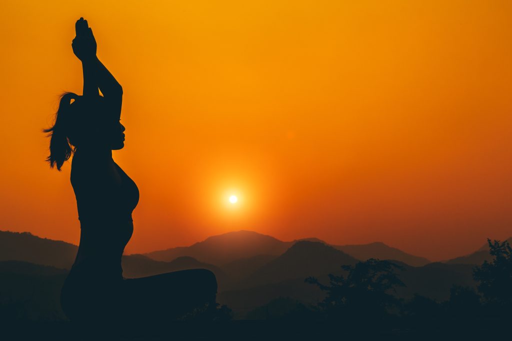 As the morning sun rises over the hills and trees, a girl practices meditation in the tranquil surroundings, embracing the peaceful environment.