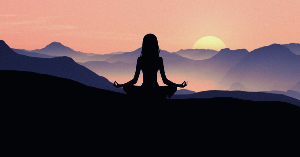 A girl sits atop a hill during a full moon yoga trek, as the moon rises over the hills. The scene is bathed in shades of black, blue, and purple, creating a serene and mystical atmosphere.