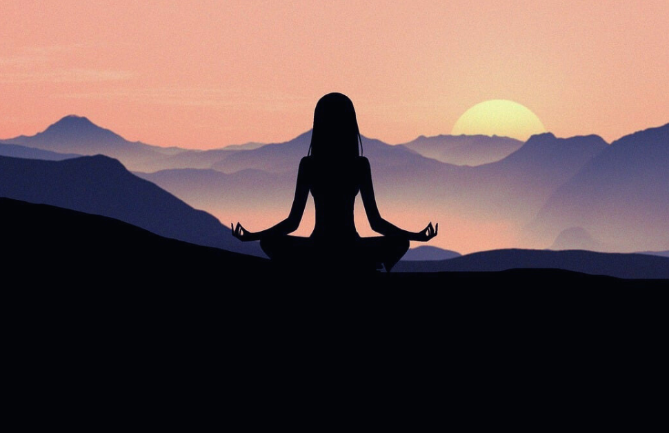 A girl sits atop a hill during a full moon yoga trek, as the moon rises over the hills. The scene is bathed in shades of black, blue, and purple, creating a serene and mystical atmosphere.