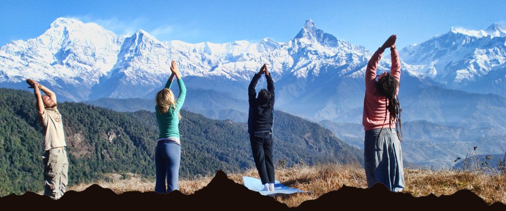 In the image, people are practicing yoga in the Namaskar pose on a mat atop a hill, surrounded by dry grass. The breathtaking backdrop features snow-capped Himalayan peaks, with lush green forests visible on the lower hills. This serene setting beautifully combines the peace of nature with the spiritual practice of yoga.