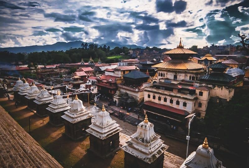 on the left hand side we can see the steps and down the steps there is 9 small temples  and again there is steps to go to river Bagmati and across the river there we can see the many people as well as there is houses and the temple of "Pashupatinath" in the center and surrounded by the many houses and temples 