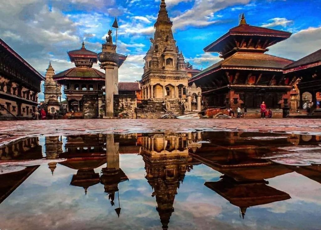 in the picture we can see the three different architectural designs of temple  and their reflection is seen on the water which is on the center and we can see the blue sky and people are sitting aside.