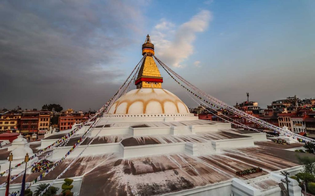 Under the blue sky we can see the bouddha stupa in which from the top of the stupa the rope is attached to the pillar with the beautiful small flags on the rope  