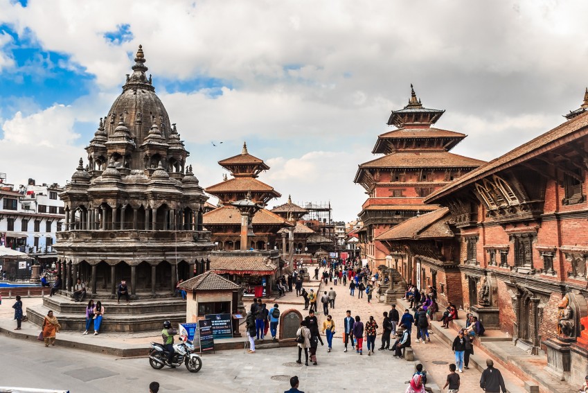 under the blue and cloudy sky there is a Krishna mandir and pyagoda style temples around the street and people are walking and riding on the street a