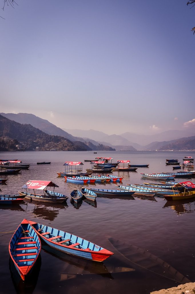 The image shows a lovely lake with many colorful boats docked in the water. The boats are bright shades of blue, red, and yellow, adding a vibrant touch. The lake is calm and mirrors the mountains and sky above. The mountains in the background look grand and impressive. Overall, the scene is peaceful and serene, highlighting the beauty of nature and the calmness of the lake.