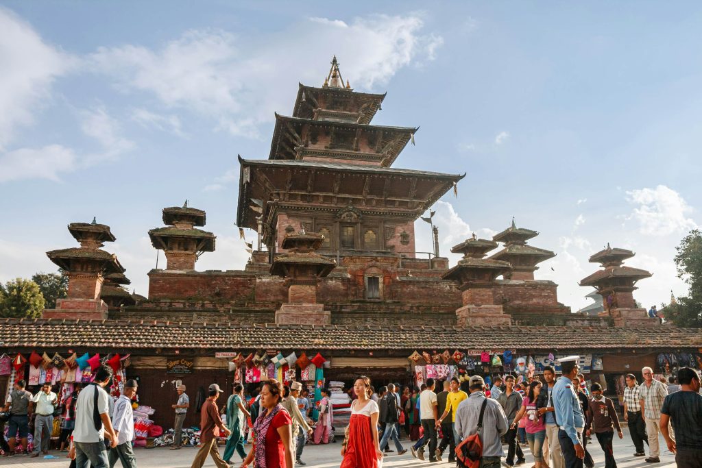 the picture is about the "Taleju Bhawani" temple which is under  the blue sky and is three -storey temple alongside the temple there is the path for the people where the different people re walking  