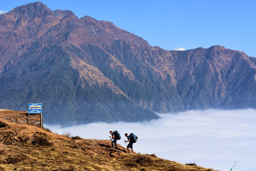 Two men are trekking the Annapurna Circuit, walking through an area where dry grasses cover the ground, while green hills rise up beside them.